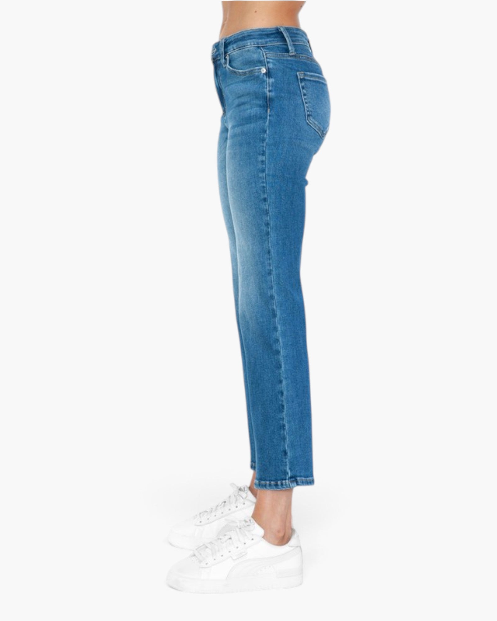A side profile view of a person wearing blue cropped denim jeans and white sneakers against a plain white background.