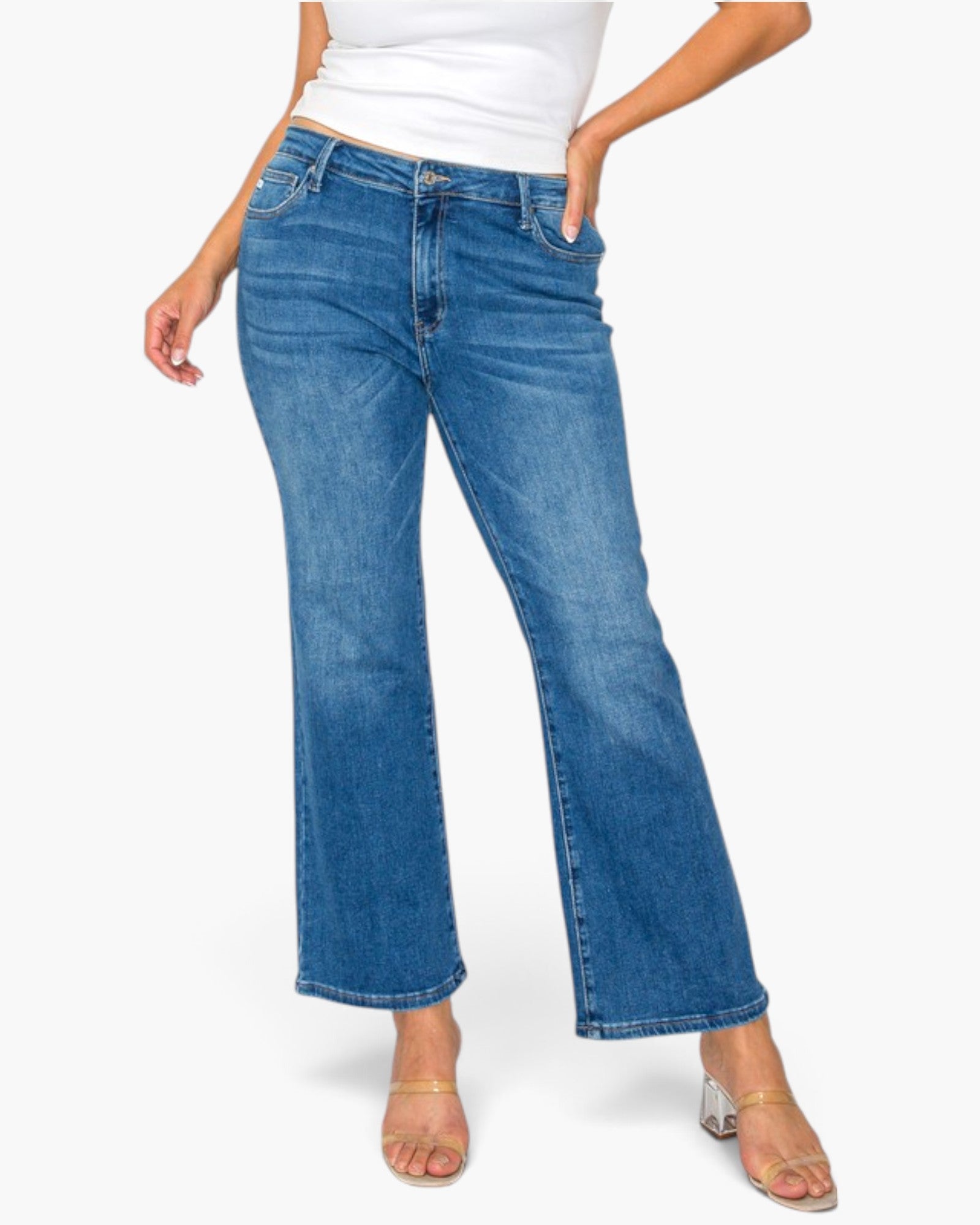 A model wearing a pair of medium-wash blue flare jeans, styled with a white top and clear block-heel sandals, against a plain white background.