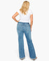 A woman viewed from the back wearing light-wash blue flare jeans, a white short-sleeve T-shirt, and brown shoes against a plain white studio background.