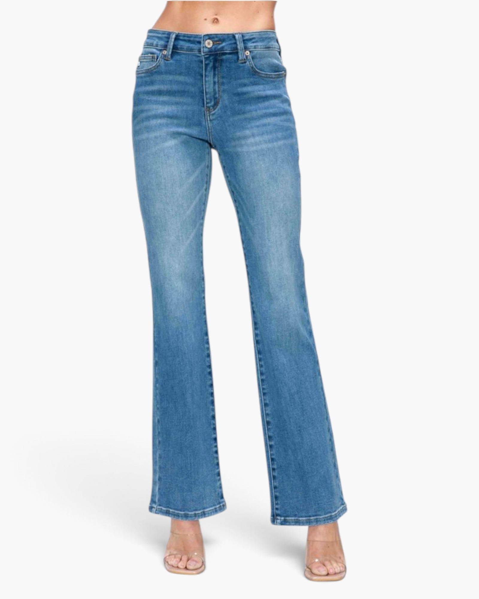 A pair of medium-wash blue denim flare jeans shown on a model from the waist down, paired with clear high-heel sandals against a plain white studio background.