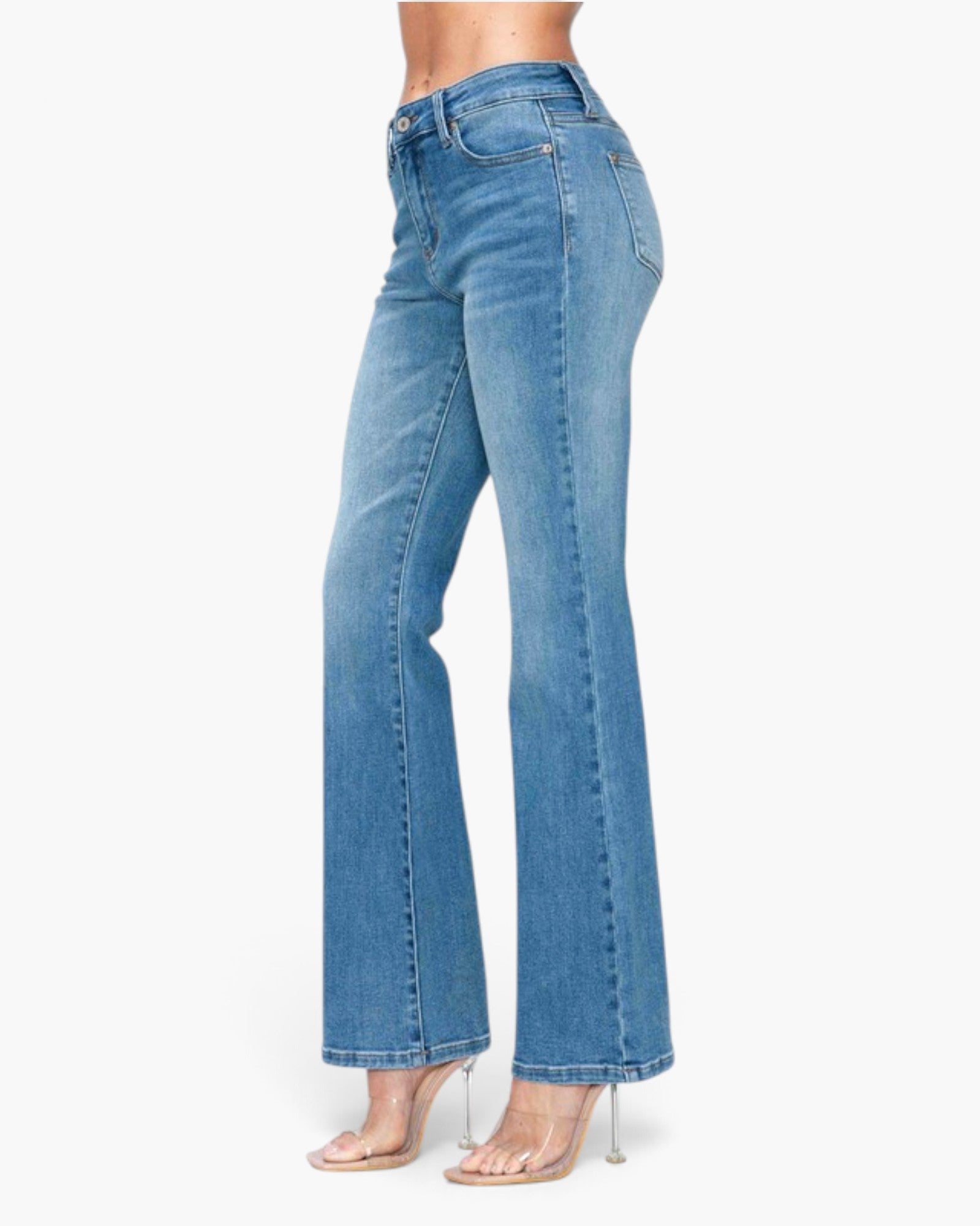 A model wearing a pair of high-waisted, light blue flare jeans with clear high-heeled sandals, shown from a side profile against a plain white background.