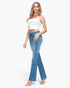 A woman modeling a white cropped camisole top and light blue high-waisted flare jeans with decorative side cutouts, paired with clear high-heeled sandals, against a plain white studio background.