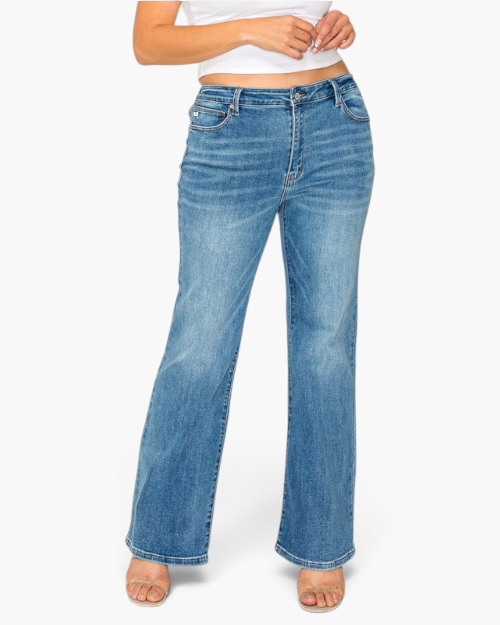 A person wearing light blue high-waisted flare jeans with a white cropped top and beige sandals, shown from the waist down against a plain white studio background.