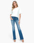 A woman modeling a white short-sleeve t-shirt and blue flare jeans with a faded wash, standing against a light gray studio background.