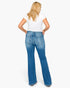 A woman viewed from behind wearing blue flare jeans and a white t-shirt, standing against a plain white studio background.