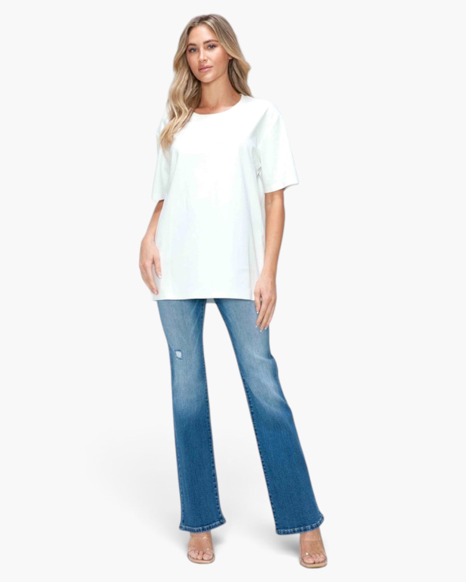 A woman modeling a white short-sleeve crewneck t-shirt and blue flare jeans against a plain white background.
