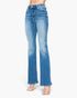 A model is wearing a pair of high-waisted, light blue flare jeans with a subtle faded wash and a small distressed detail on the left thigh, paired with clear high-heeled sandals against a plain white background.