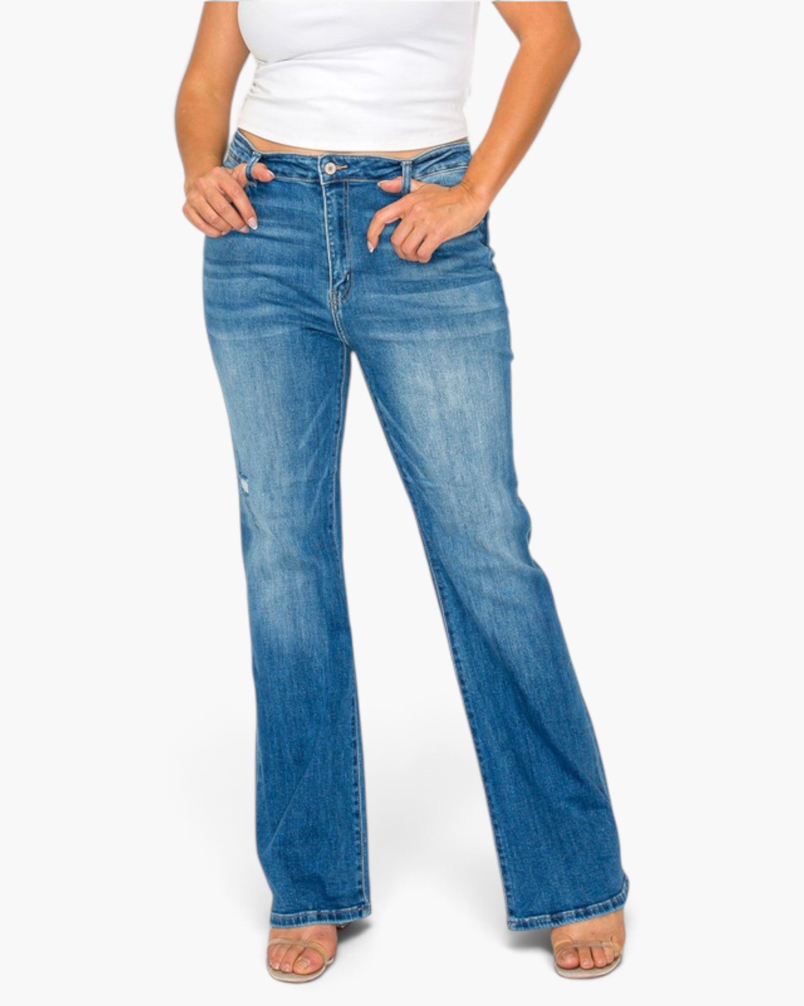 A model wearing a pair of medium-wash blue denim jeans with a slight flare, paired with a white cropped top and flat sandals, against a plain white background.