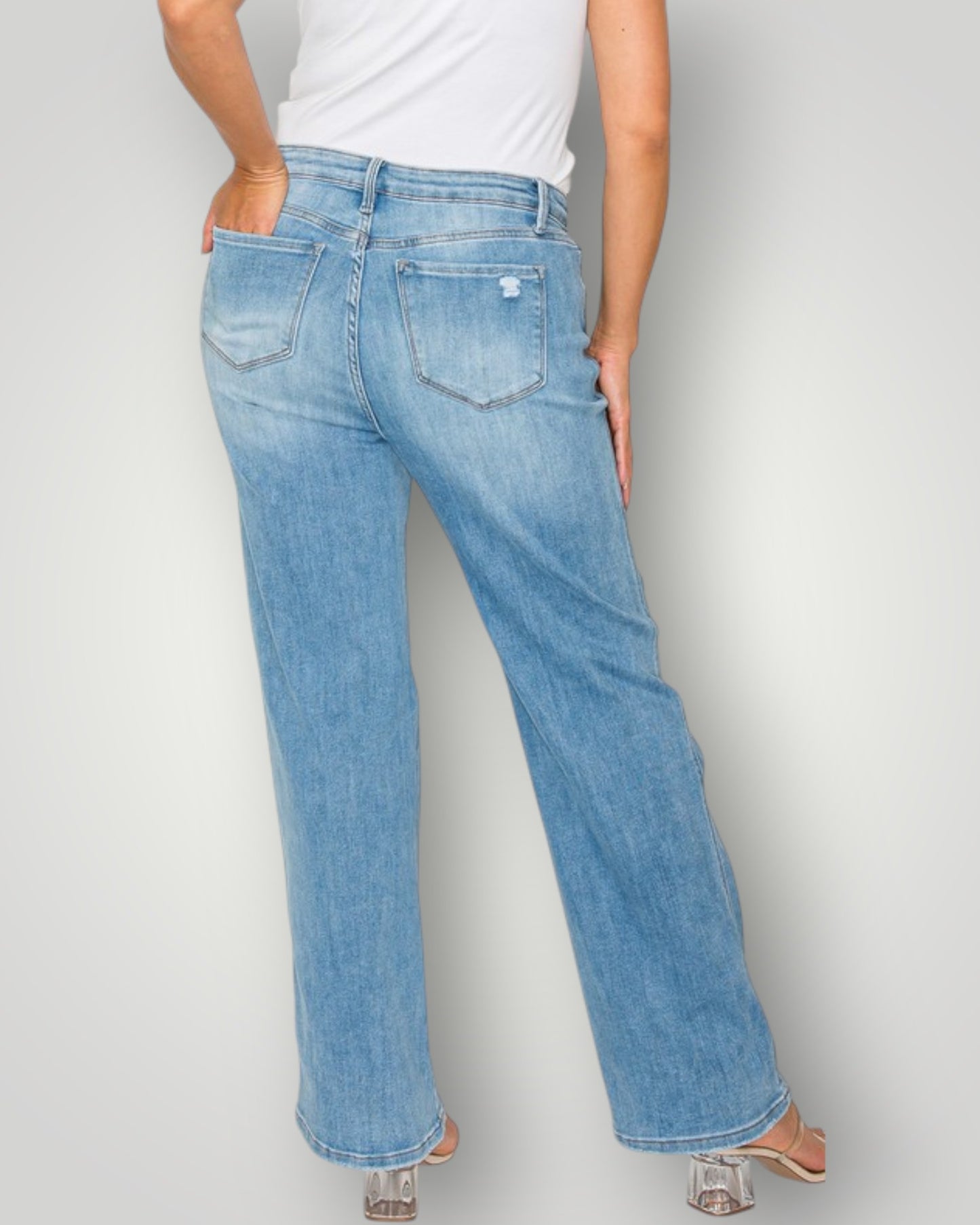 Person wearing light blue jeans and a white top on a plain background