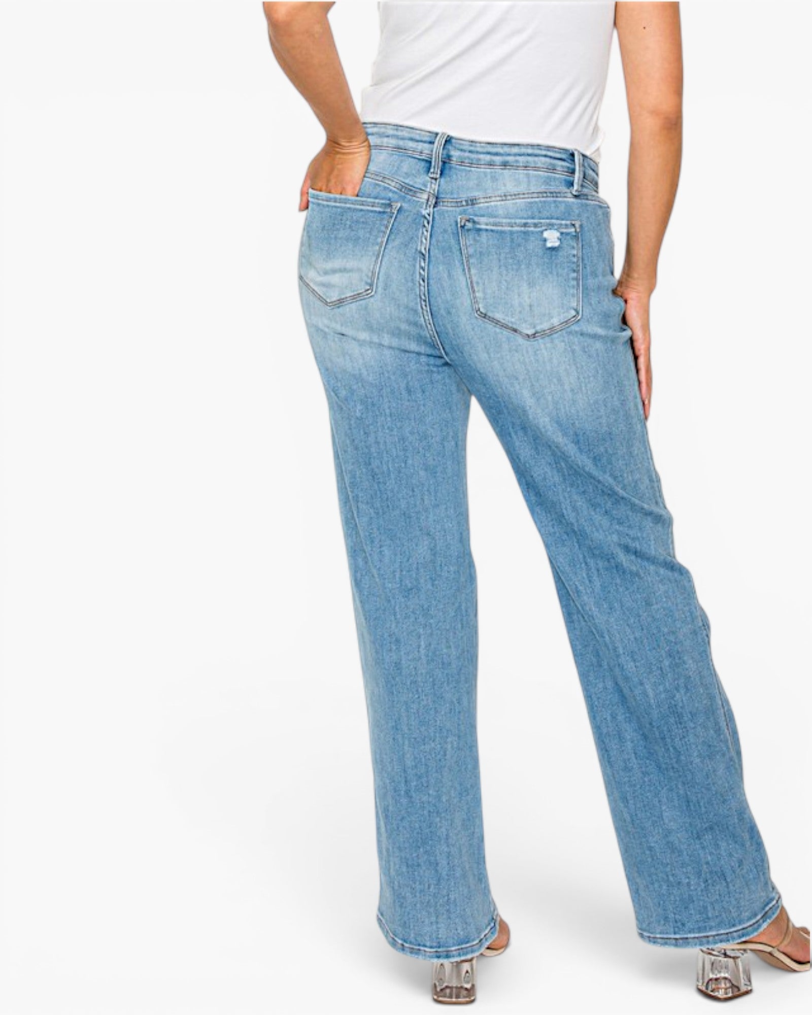 A person shown from the back wearing light blue wide-leg jeans with a white top and clear high-heel sandals against a plain white studio background.