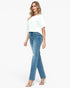 A woman modeling a pair of light-wash blue skinny jeans with distressed details on the thighs, paired with a white t-shirt and clear high-heeled sandals, against a plain white background.