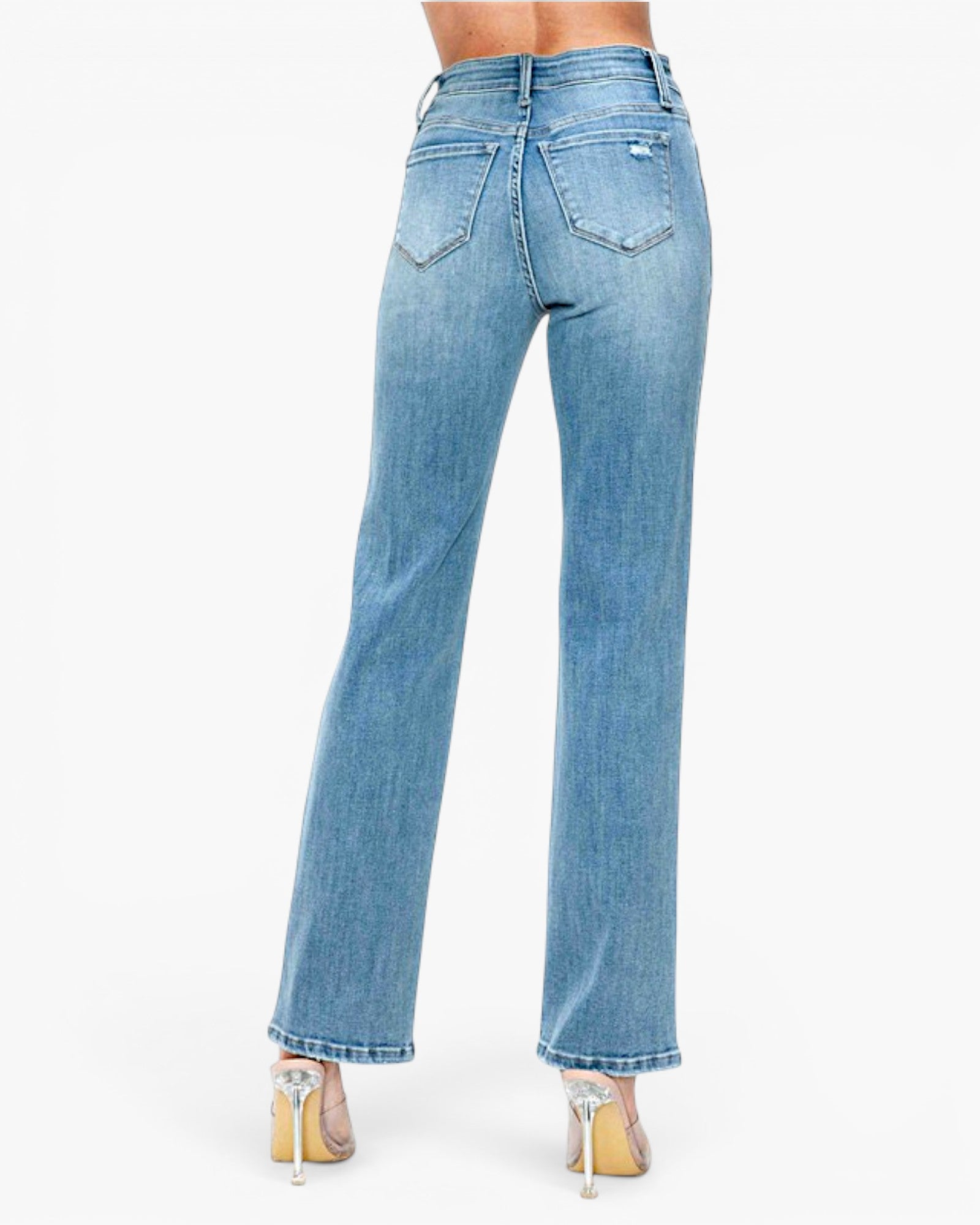 Rear view of a model wearing light blue high-waisted straight-leg jeans with a slight flare, paired with clear high-heeled sandals, against a plain white background.