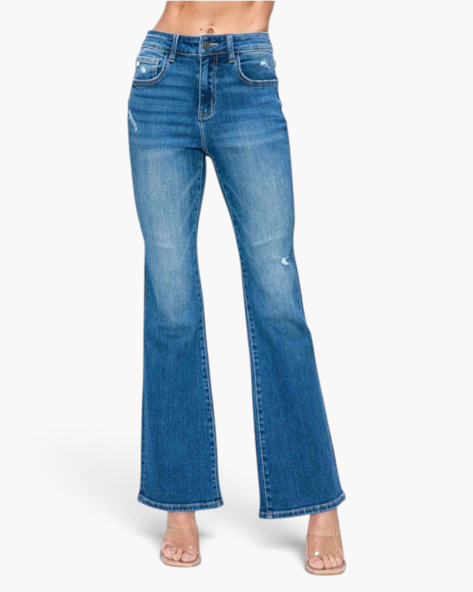 A model wearing a pair of medium-wash blue denim flare jeans with distressed details on the thighs and knees, paired with clear high-heeled sandals against a plain white background.