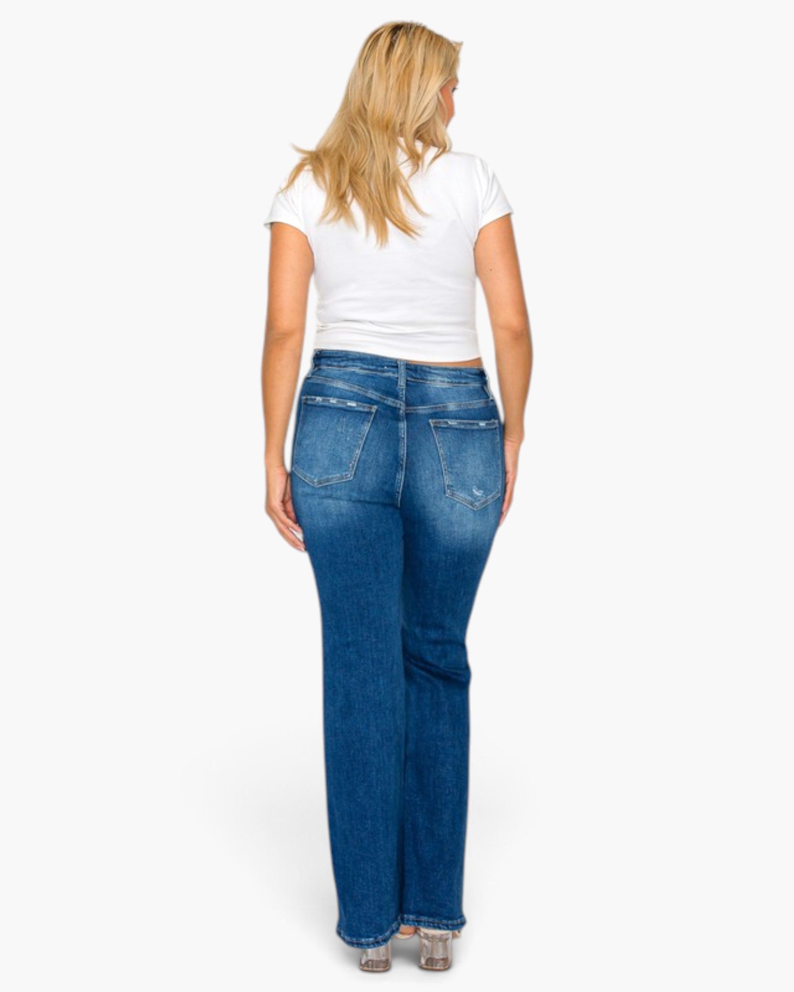A woman viewed from the back wearing blue straight-leg jeans, a white short-sleeve t-shirt, and clear high heels against a plain white studio background.