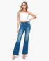A woman modeling a pair of high-waisted, blue flare jeans with a white cropped camisole top, standing against a plain white studio background.