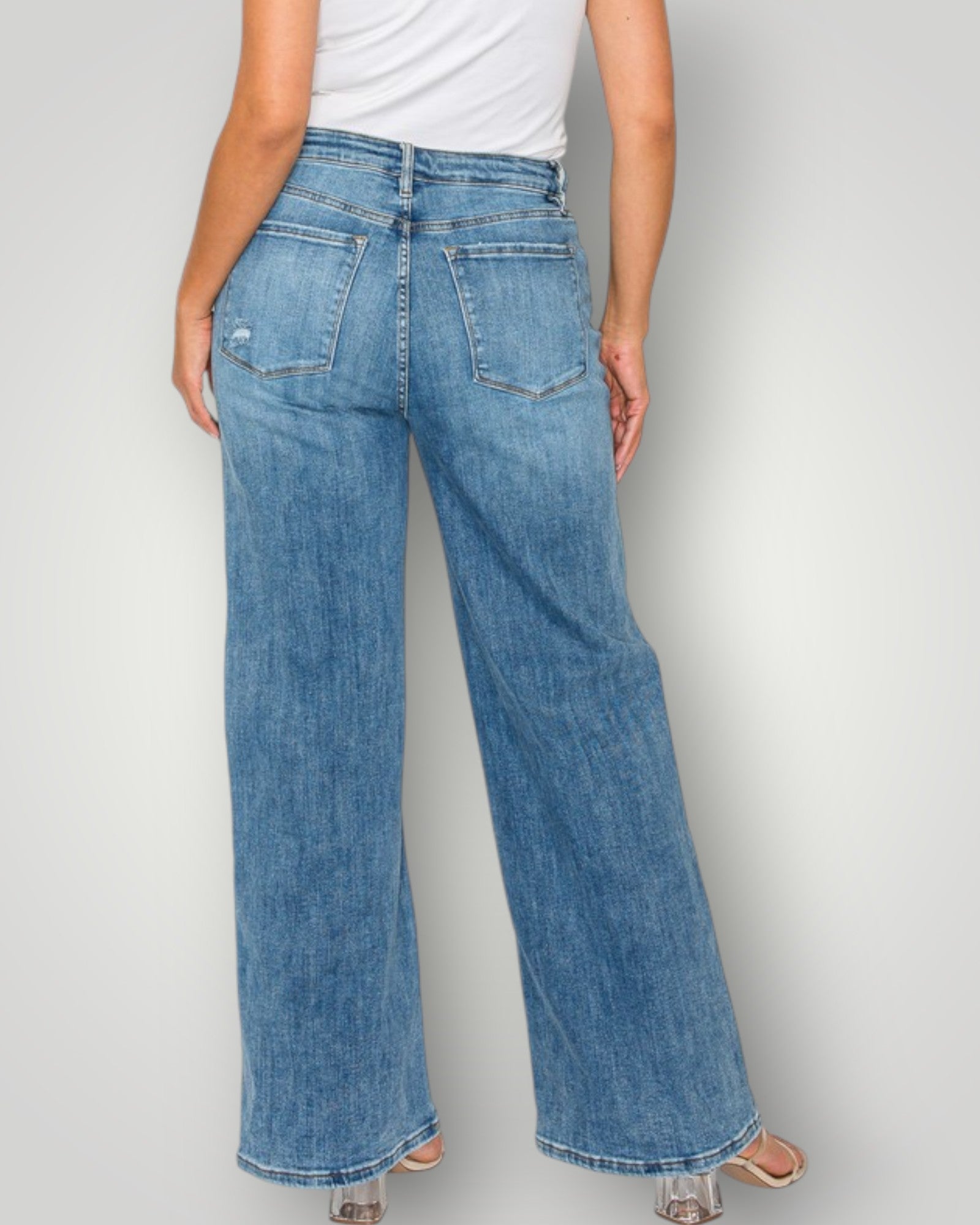 Person wearing blue jeans and a white top on a plain background