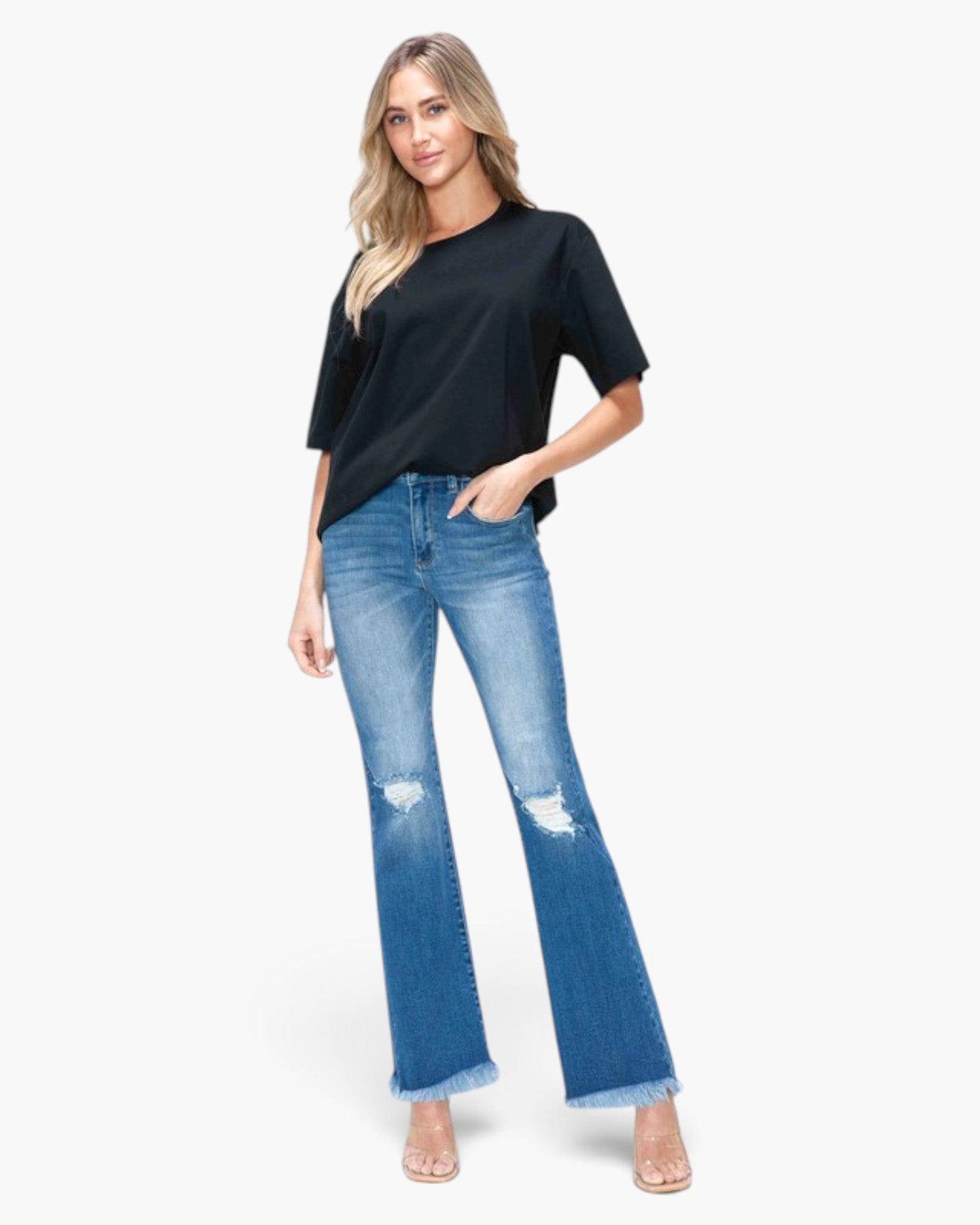 A woman modeling a black short-sleeve t-shirt and blue distressed flare jeans with frayed hems, standing against a plain white studio background.