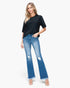 A woman modeling a black short-sleeve t-shirt and blue distressed flare jeans with frayed hems, standing against a plain white studio background.