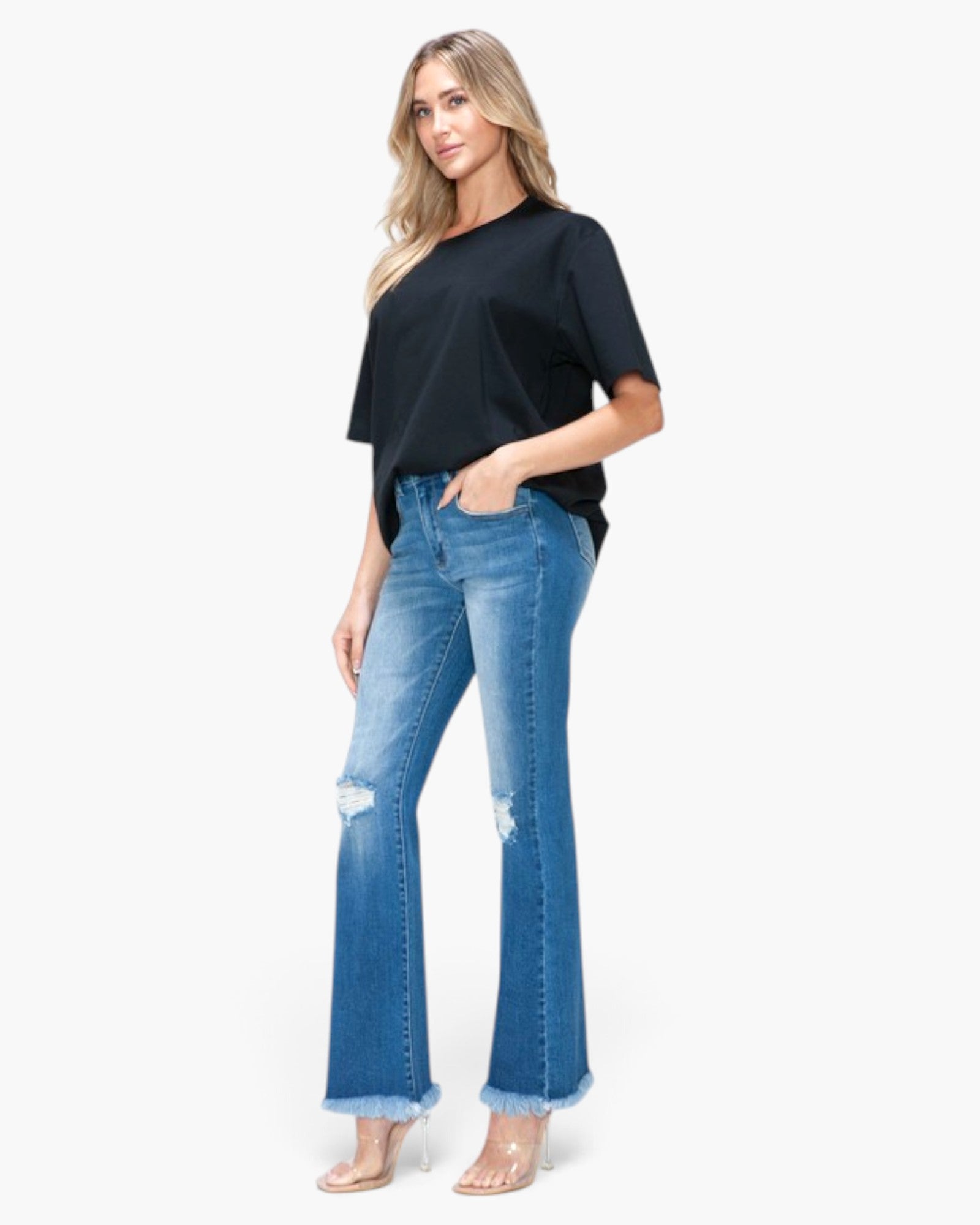 A woman modeling a black short-sleeve top and blue distressed flare jeans with frayed hems, standing against a plain white studio background.