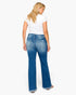 A woman shown from the back wearing blue flare jeans with a white t-shirt, standing against a plain white background.