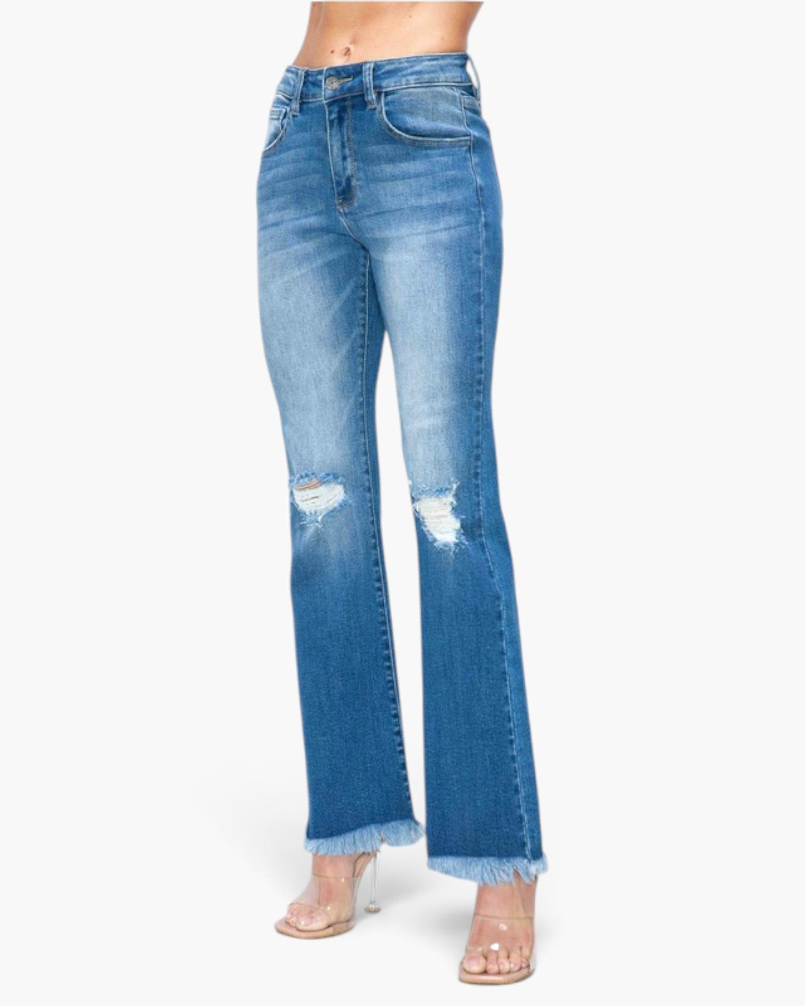 A model wearing a pair of medium-wash blue denim flare jeans with distressed rips on the thighs and frayed hems, paired with clear high-heel sandals against a plain white background.