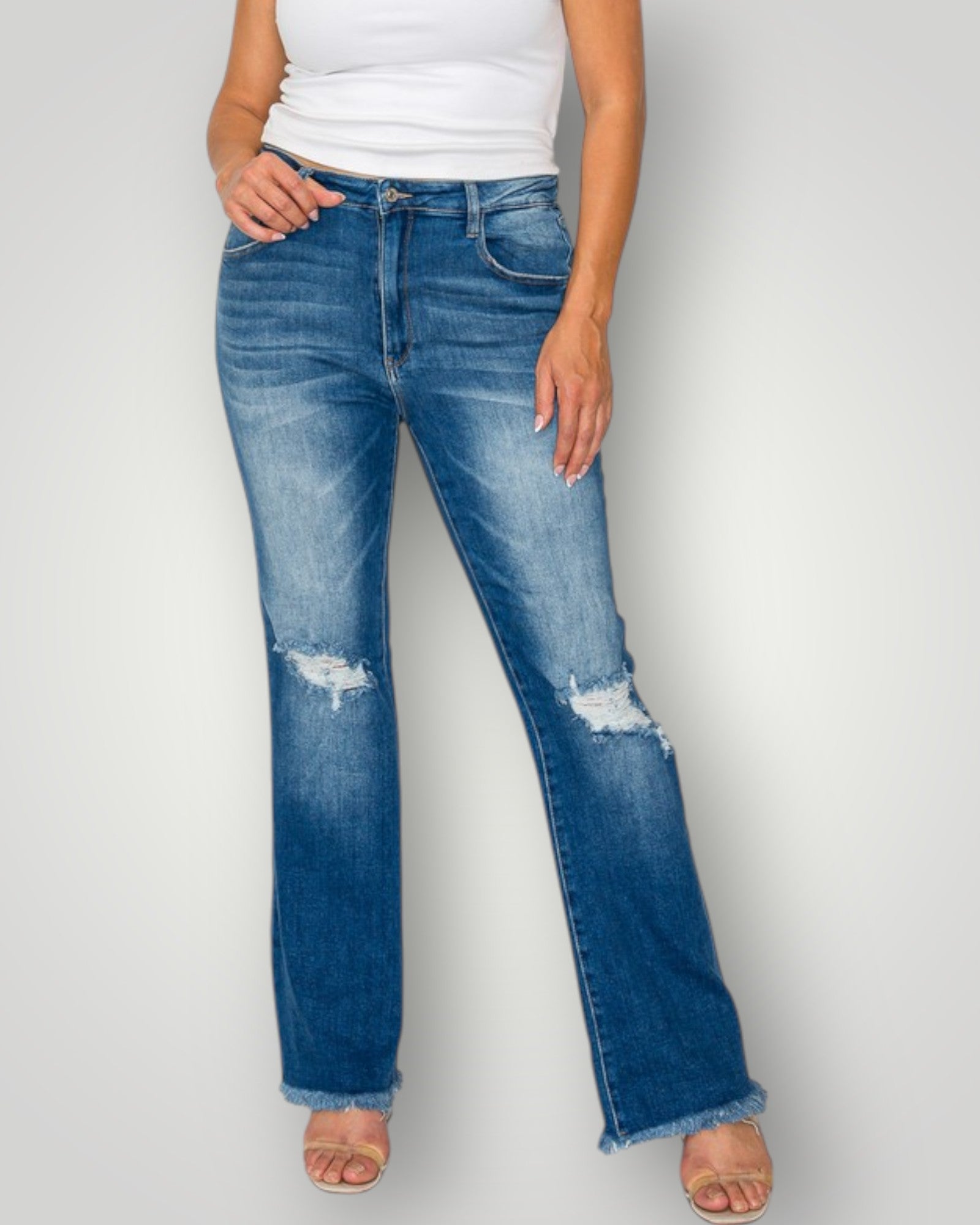 Person wearing blue jeans with slight distressing on a plain background
