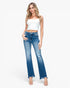 A woman modeling a pair of medium-wash blue flare jeans with a faded wash and distressed details, paired with a white crop top and clear high-heeled sandals, against a plain white background.