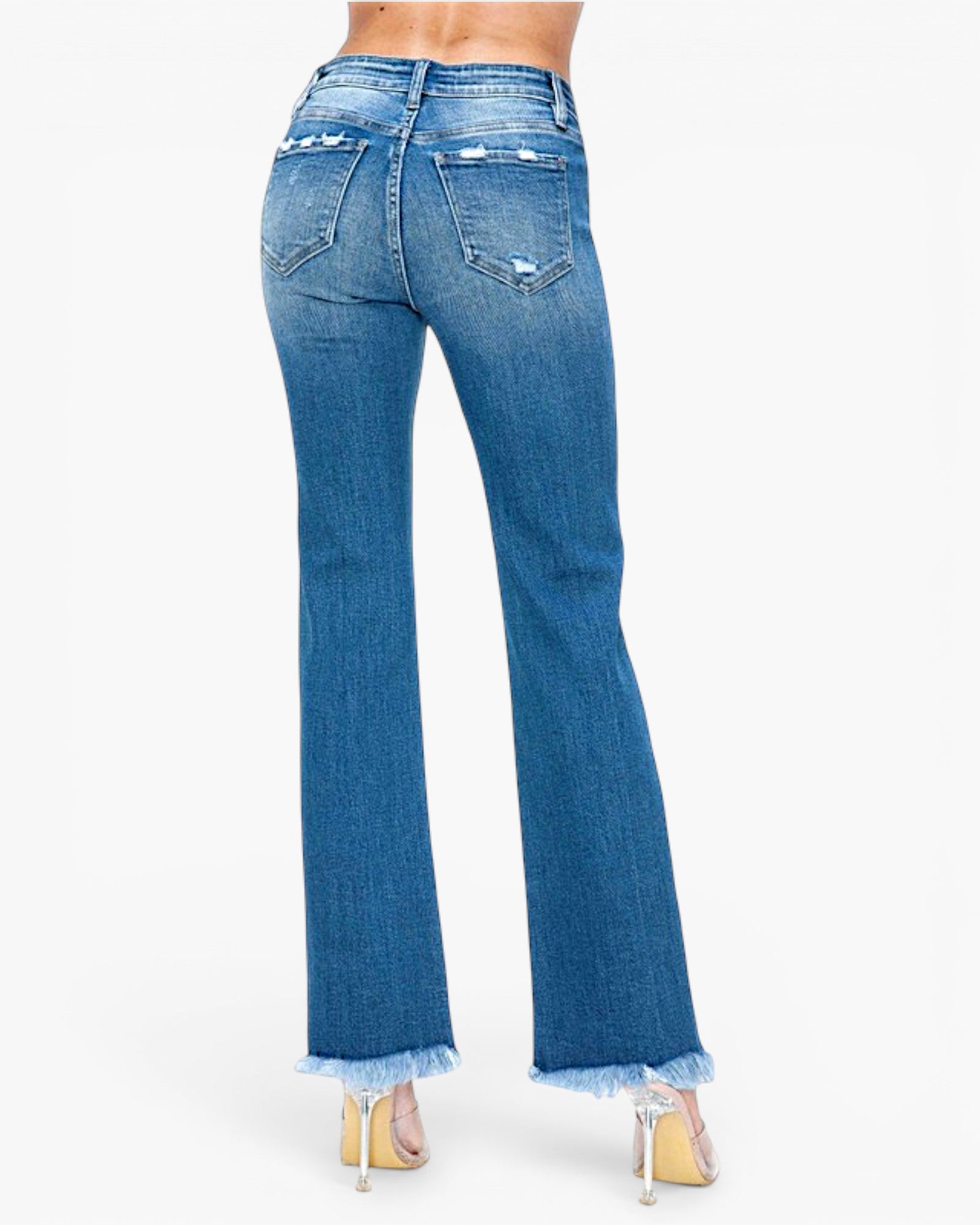 Rear view of a person wearing blue flare jeans with a frayed hem and distressed details on the back pockets, paired with clear high heels against a plain white background.