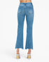 Back view of a model wearing light blue cropped flare jeans with a frayed hem and metallic high heels against a white studio background.