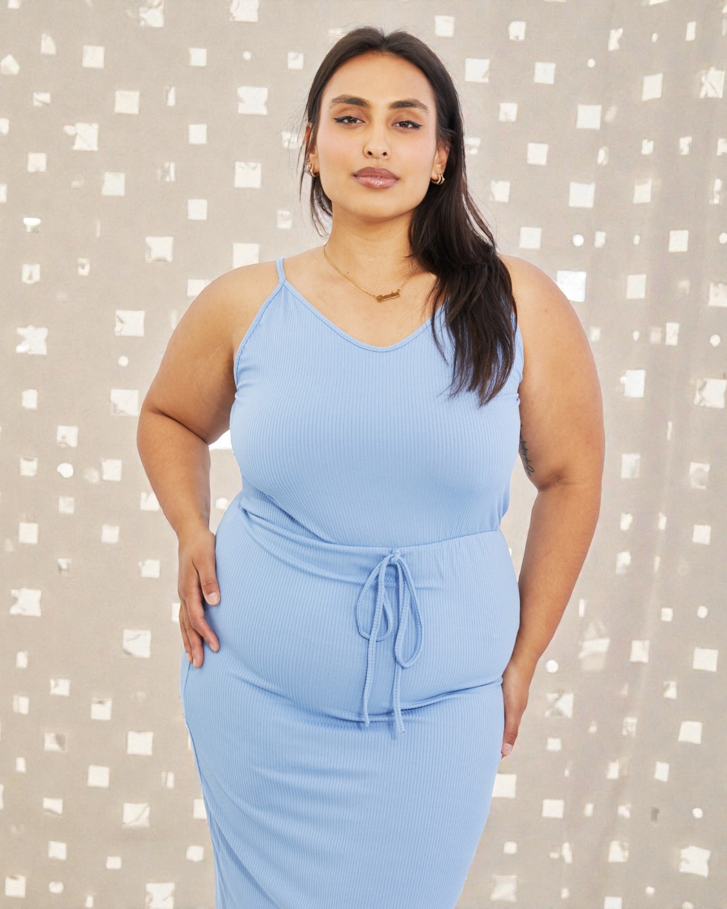 Woman wearing a light blue sleeveless dress against a patterned background