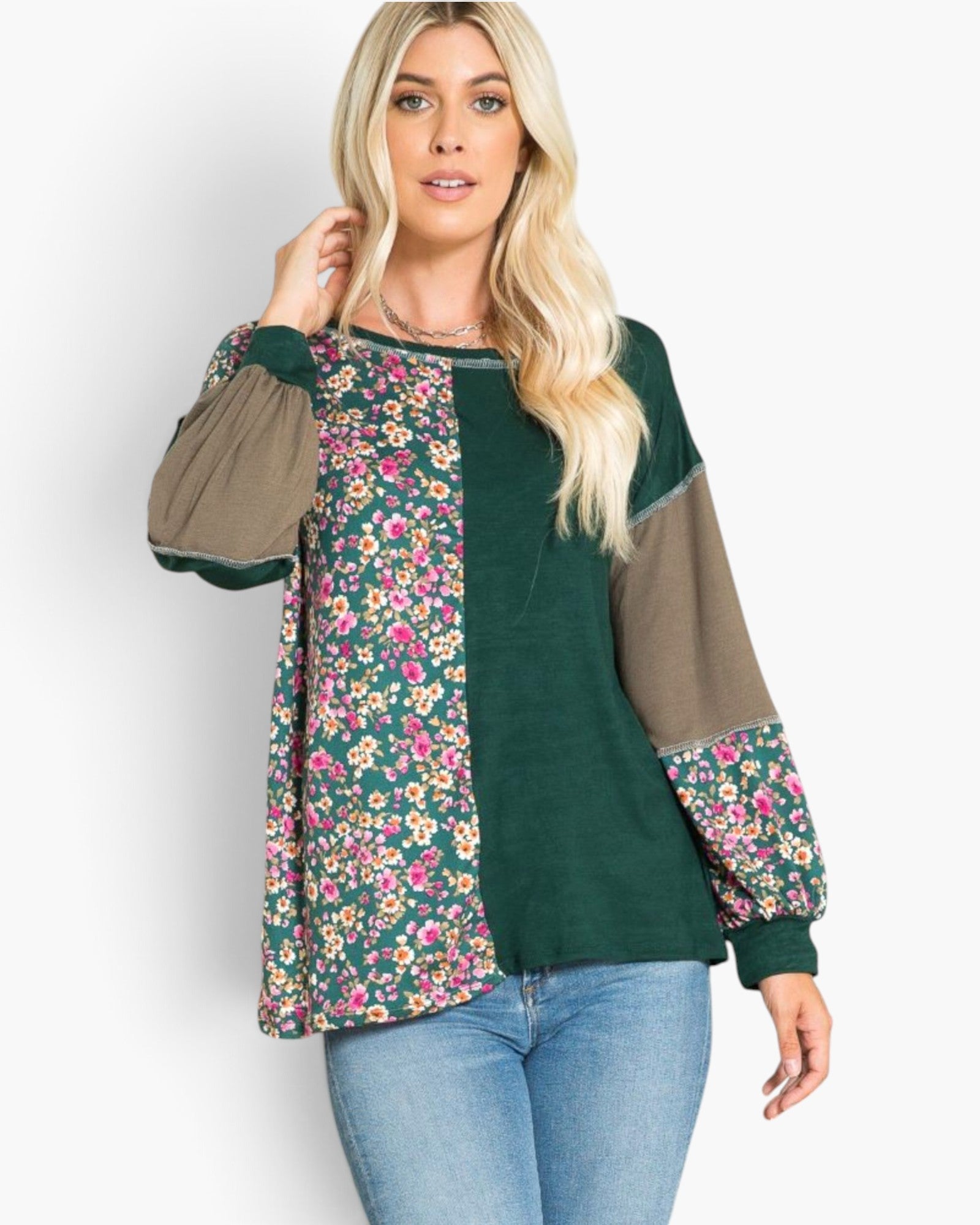 A woman modeling a color-blocked long-sleeve top with a dark green base, olive-brown sleeves, and pink and yellow floral patterns on the front panels, paired with blue jeans against a light gray background.
