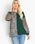 A woman modeling a color-blocked long-sleeve top with a dark green base, olive-brown sleeves, and pink and yellow floral patterns on the front panels, paired with blue jeans against a light gray background.