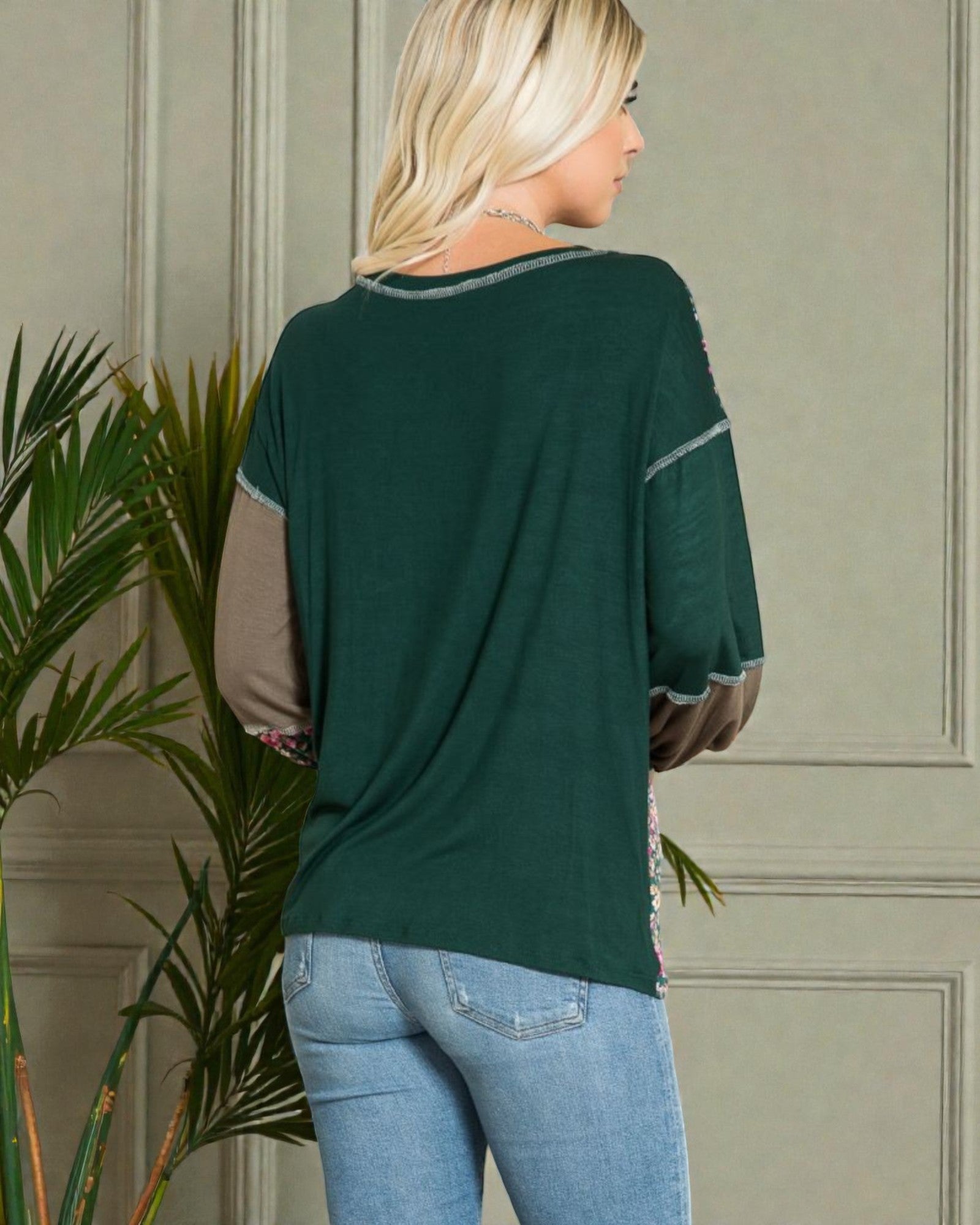 Woman wearing a green and beige top with a plant in the foreground
