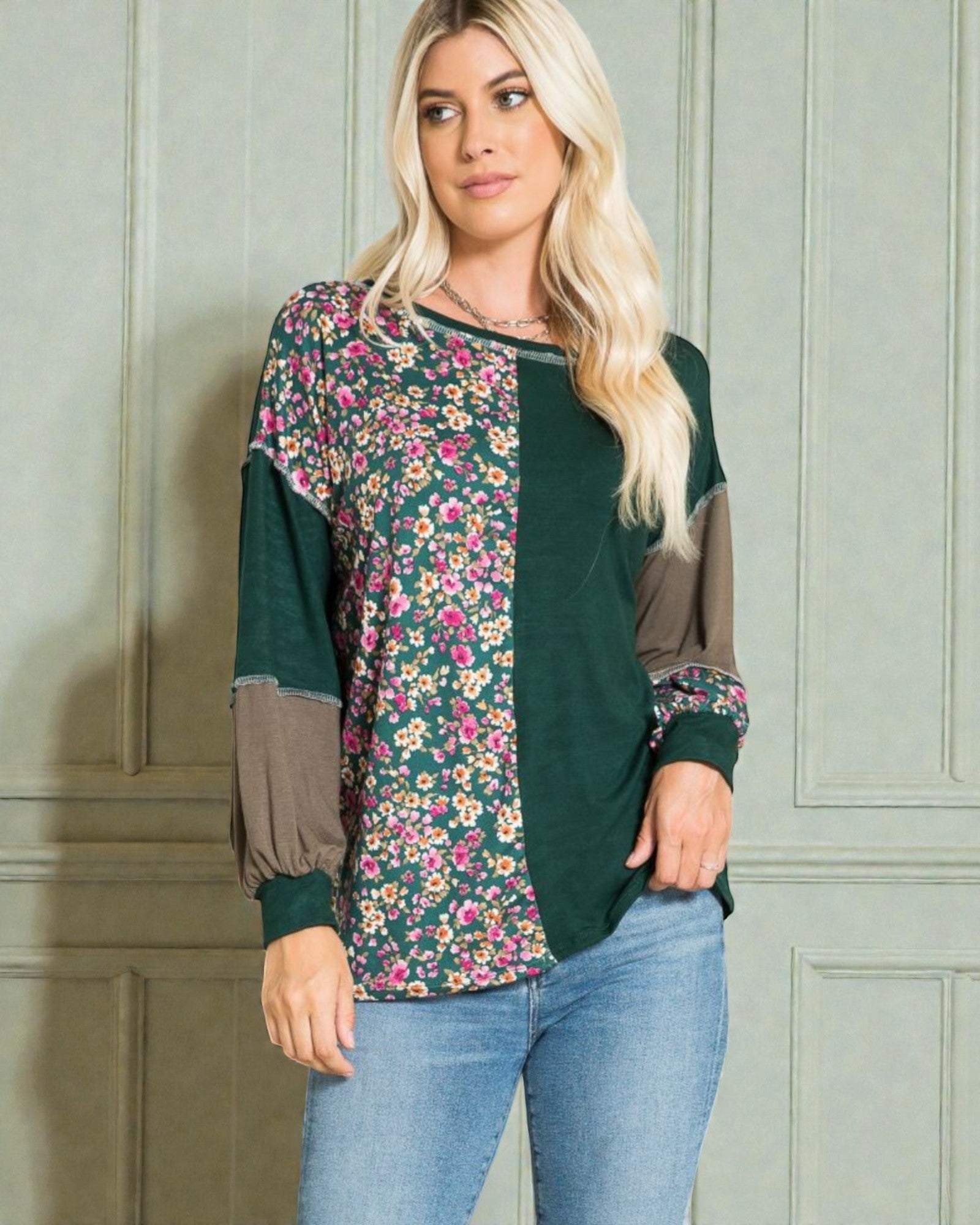 Woman wearing a green and floral-patterned top against a light gray wall.