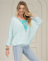 Woman wearing a light blue blouse with floral embroidery and jeans, standing against a neutral background.