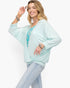 A woman modeling a light mint green kimono-style cardigan over a turquoise floral top and light blue jeans, accessorized with bracelets, against a plain white background.