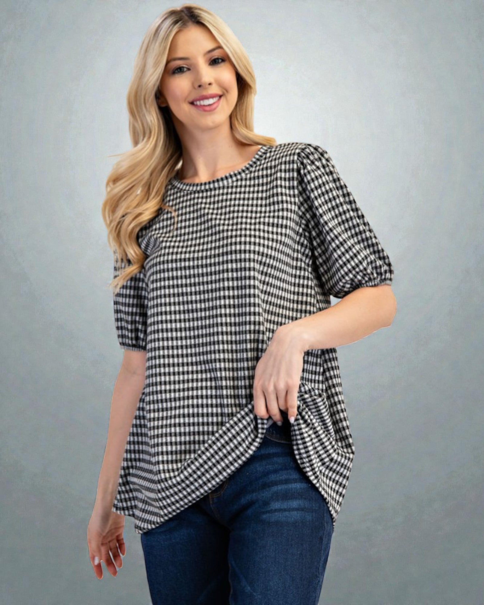 Woman wearing a black and white checkered blouse with blue jeans on a gray background