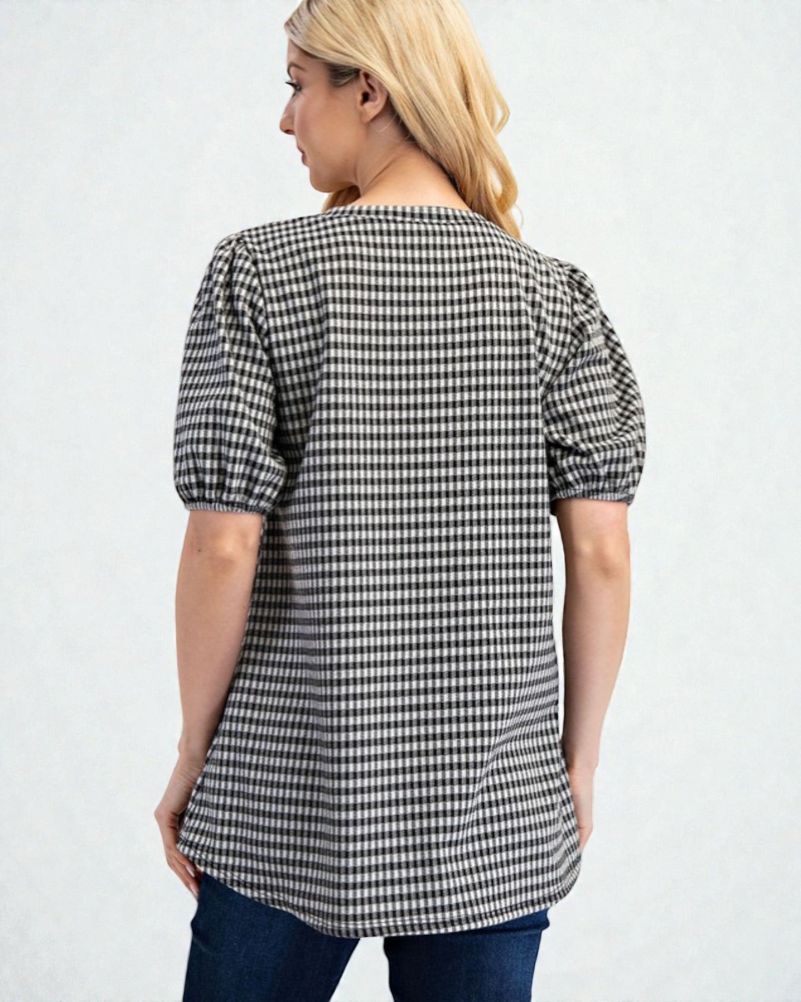 Woman wearing a black and white checkered blouse with puff sleeves on a light gray background