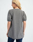 Woman wearing a black and white checkered blouse with puff sleeves on a light gray background