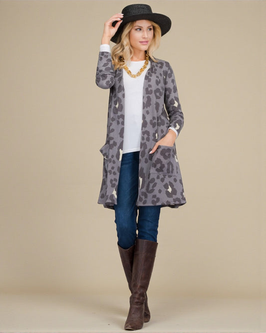 Woman wearing a gray leopard print cardigan, blue jeans, and brown boots against a beige background