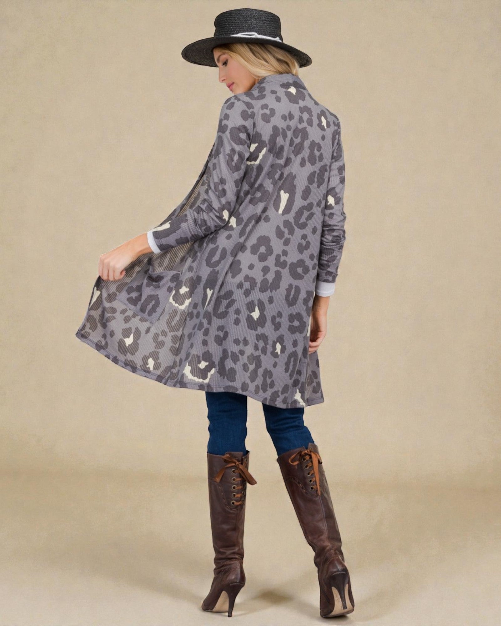 Woman wearing a gray leopard print coat with brown knee-high boots and a black hat on a beige background