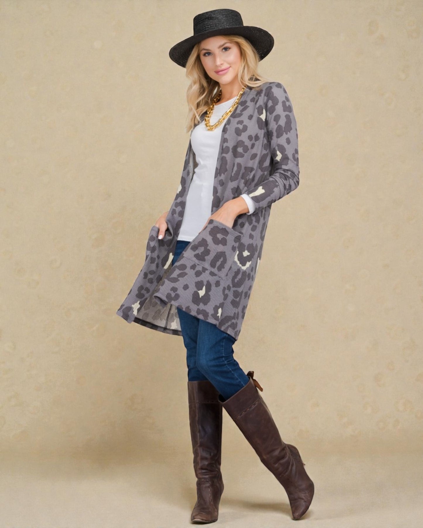 Woman wearing a leopard print cardigan, white shirt, blue jeans, and brown knee-high boots against a beige background.
