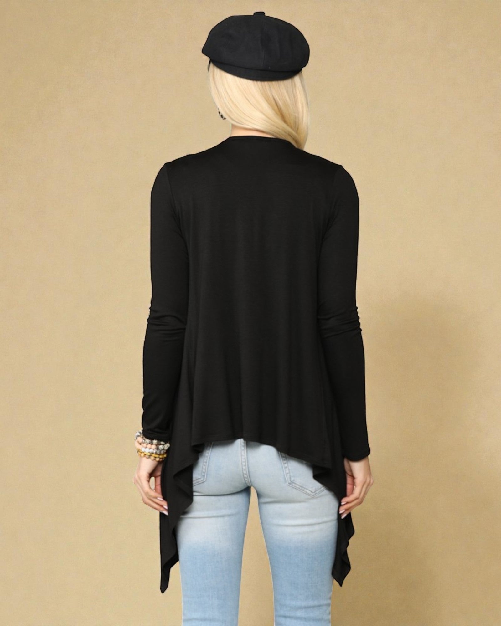 Person wearing a black long-sleeve top and light blue jeans with a beige background