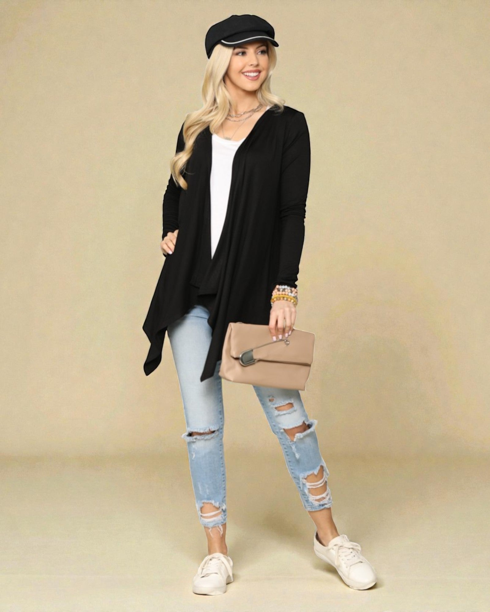 Woman wearing a black cardigan, white top, light blue ripped jeans, and white sneakers on a beige background