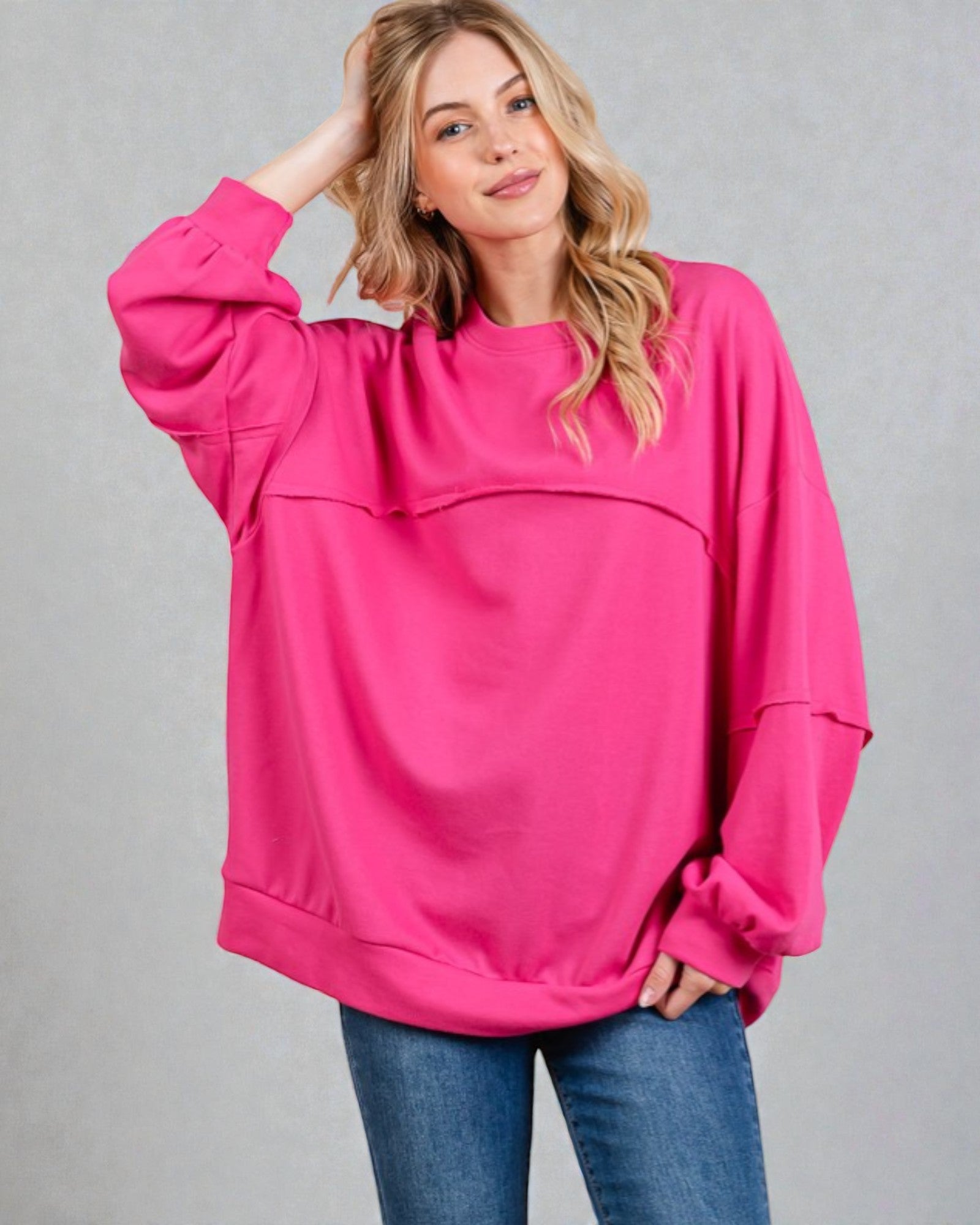 Woman wearing a bright pink oversized sweatshirt and blue jeans on a gray background