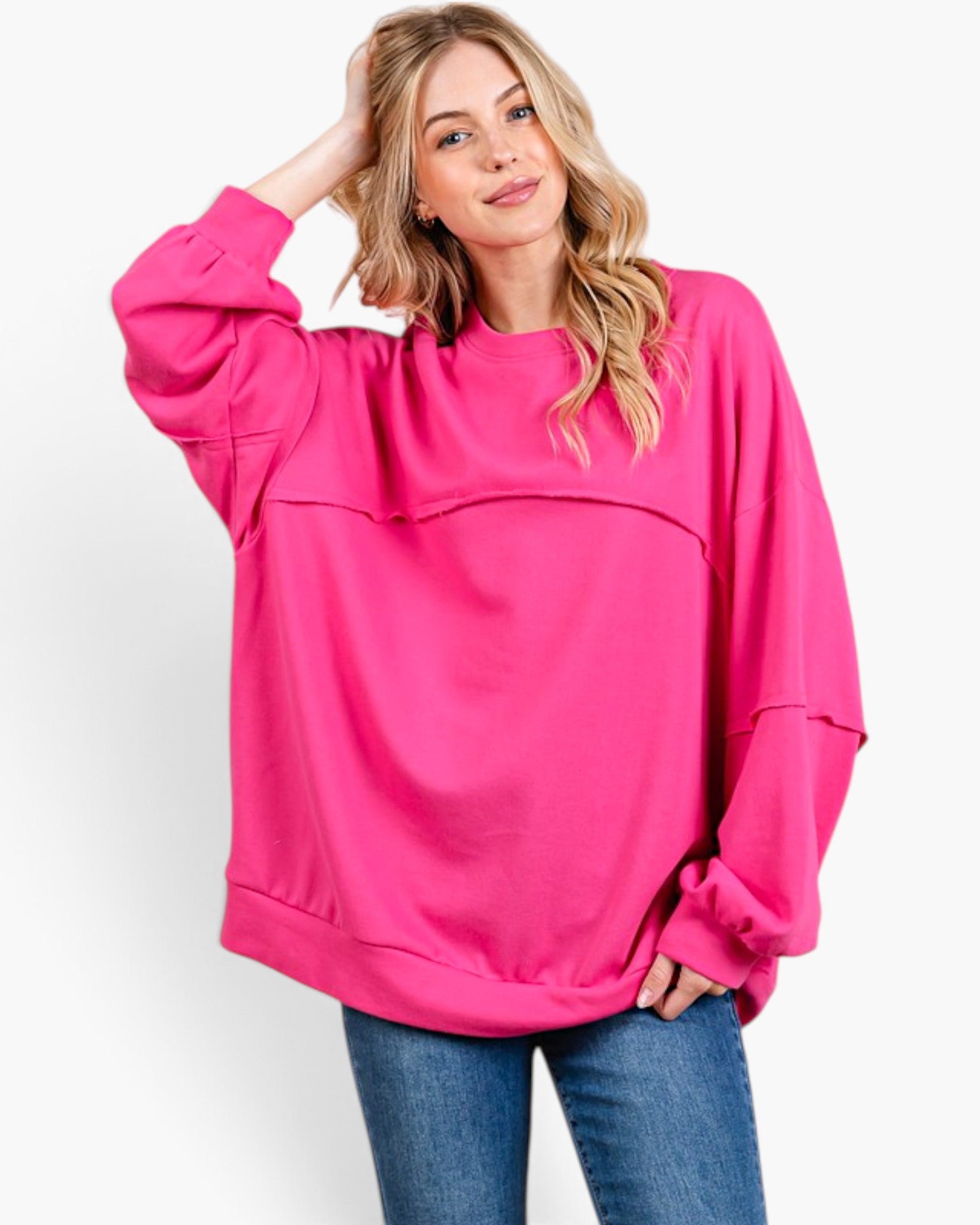 A woman modeling a bright pink oversized crewneck sweatshirt with long sleeves and a relaxed fit, paired with blue jeans against a plain white studio background.