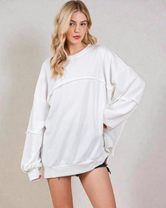 Woman wearing a white oversized sweatshirt against a plain background