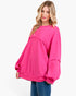 A woman modeling an oversized hot pink crewneck sweatshirt with unique layered sleeve and body details, paired with blue jeans against a plain white background.