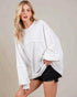 Woman wearing a white oversized sweater and black shorts on a plain background
