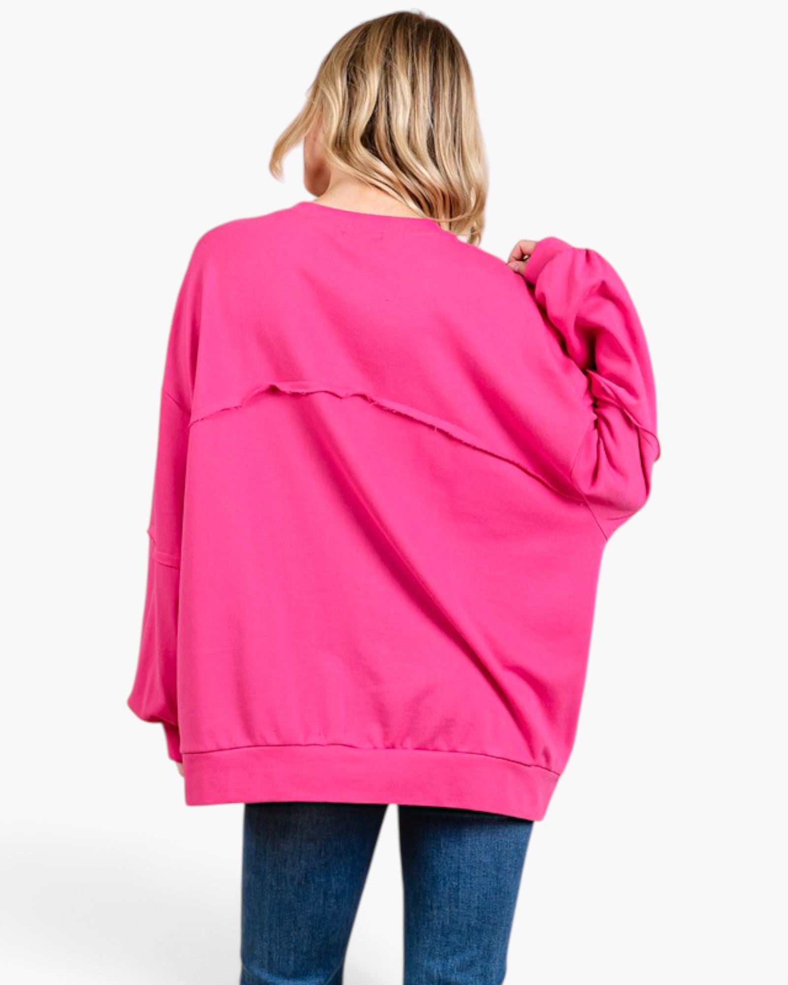 A woman viewed from behind wearing an oversized hot pink sweatshirt and blue jeans against a plain white background.